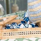Handwoven rattan Mahjong tile box with glass top, neutral tones, and island-inspired details from the Island Collection. Fits a full-size tile set. With Navy Mahjong tile set from the House Collection, featuring intricately designed tiles with floral motifs, butterflies, and peacocks. Tile size: 1" x 1 7/16" x 7/16".