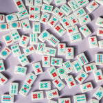 Classic white Mahjong tile set featuring colorful symbols in red, blue, and green arranged in suits and specialty tiles, displayed on a white background.